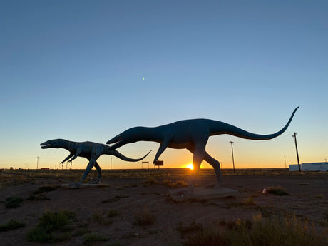 Iconic dinosaur statues silhouetted by sunset & moon. A memorable stop for your RV rental journey through the desert.
