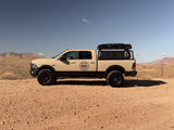 Equipped tan truck with rooftop tent parked in arid mountains; a versatile RV rental for desert adventures.