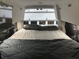 Inside an RV rental, a wide bed with gray bedding offers a comfy sleeping area for your camper van adventures.