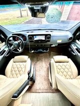 Interior of an RV rental, featuring the cockpit with a dashboard, Mercedes steering wheel, and quilted cream seats.