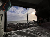 Cozy RV rental view: Sunrise/sunset over ocean, rocky shore. Feet propped on bed for ultimate relaxation.