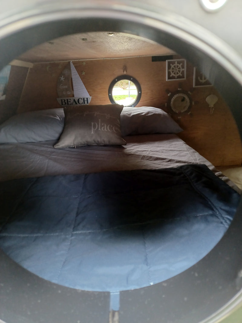 Cozy RV rental interior: bed with blue comforter, 'place' pillow, porthole window, and nautical wall decor. — photo 7