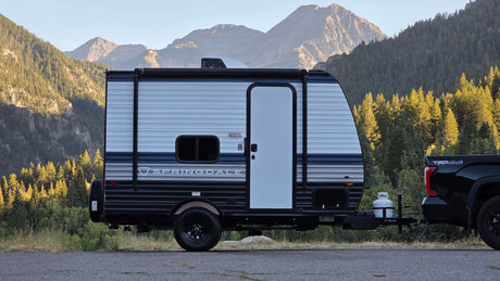 RV rental: A travel trailer and truck parked amidst scenic mountains with forests. Perfect for nature getaways.