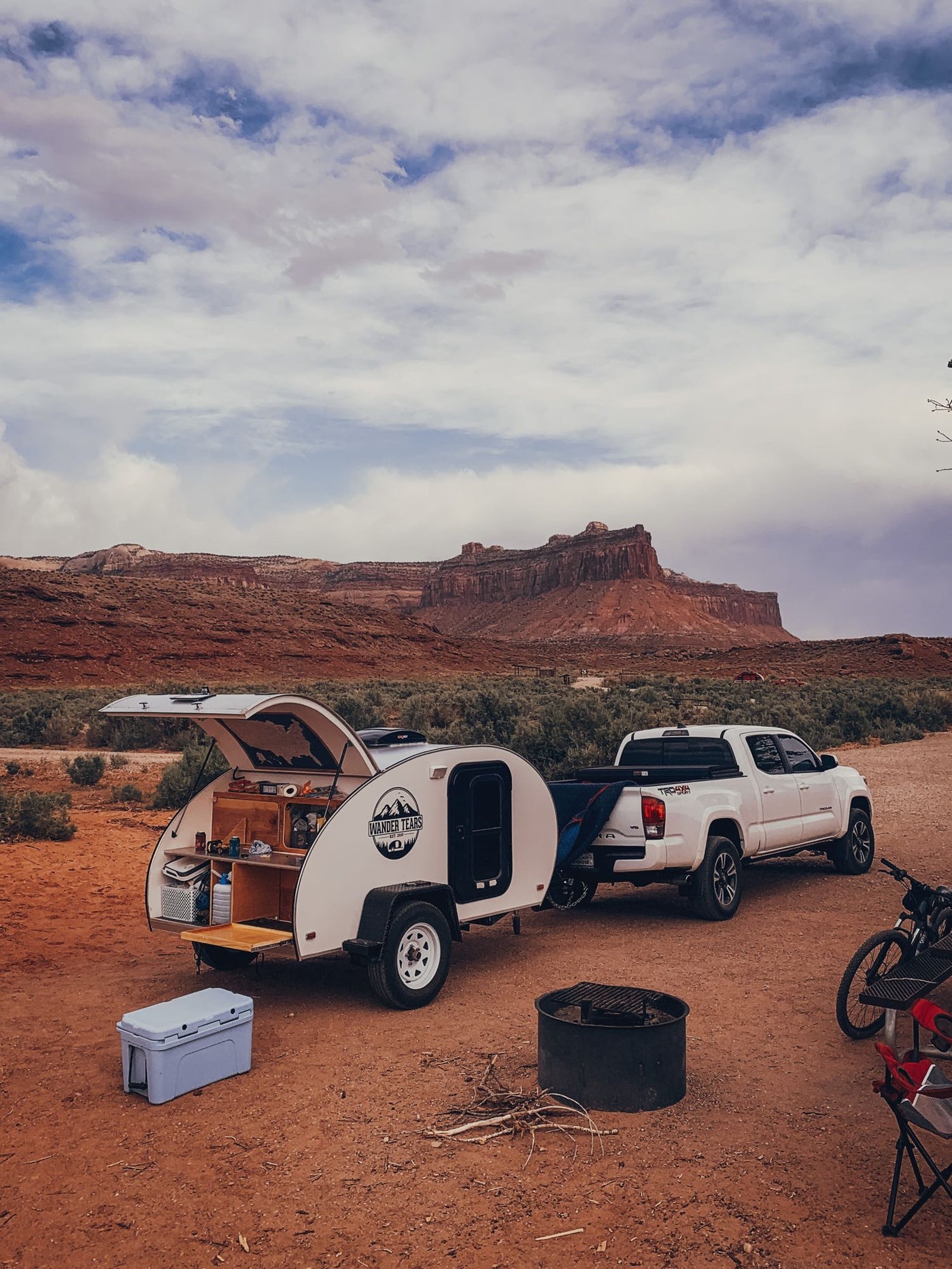 Teardrop RV rental for desert camping. White trailer with open kitchen, truck, and red rock landscape. — photo 12