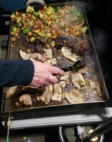 Hearty meal cooking on an outdoor griddle: fresh veggies & pork sizzle, perfect for your RV rental adventure.