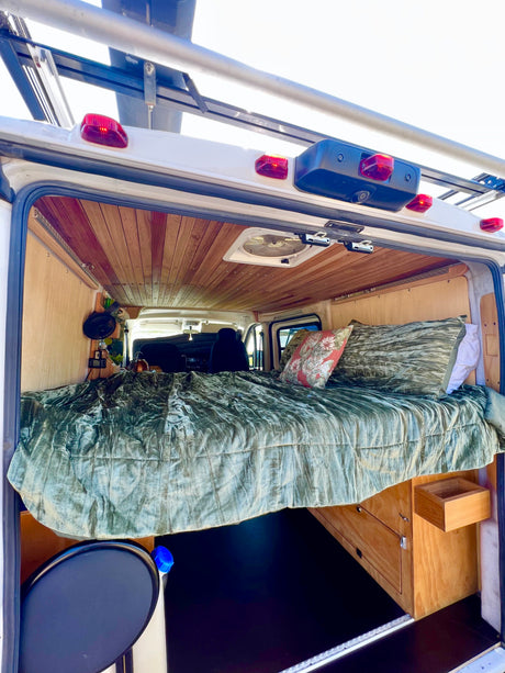 This rv rental camper van's cozy interior features an elevated bed, wood ceiling, custom storage, and front cabin view.