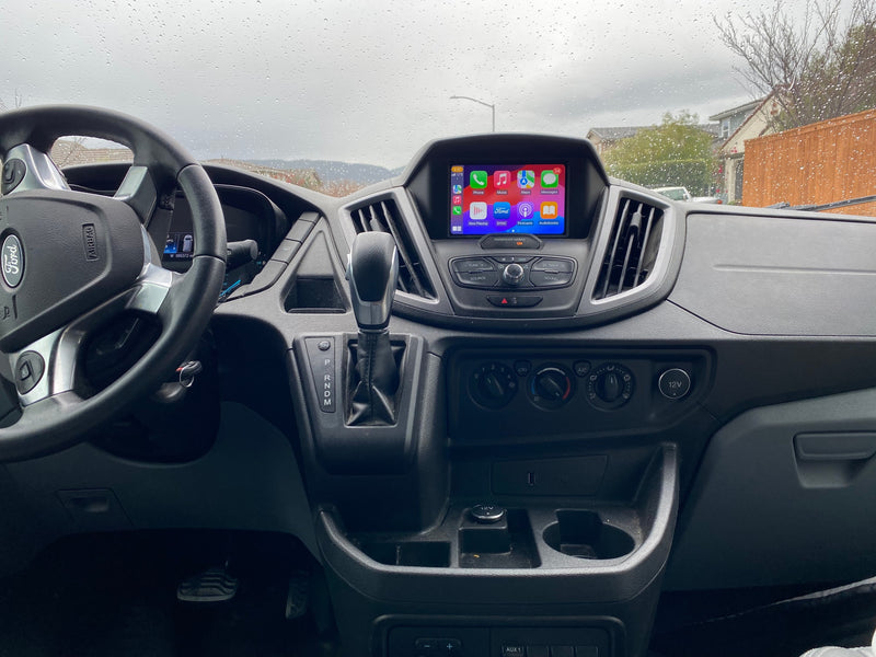 Inside a Ford Transit **rv rental** van, showing the dashboard, steering wheel, and infotainment screen with Apple CarPlay. Raindrops on windshield. — photo 16