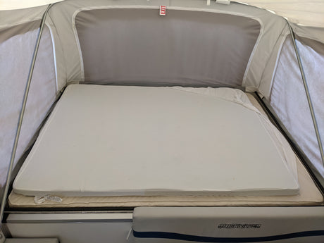 RV rental pop-up camper's interior bed: layered mattresses with an "EXIT" sign above. Quicksilver branding visible.