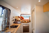 This RV rental offers a compact kitchen, cozy bed, and shower, with scenic lake views from its large window.