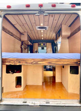 Explore van life! This cozy rv rental showcases a custom wooden interior with a comfy raised bed and smart storage.