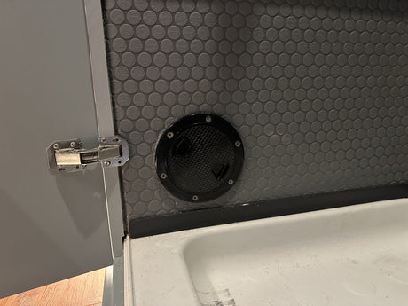 RV rental interior: Grey door with hinge, dark grey textured wall, black access hatch, and white sink below.