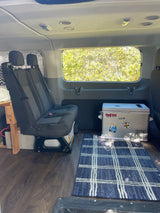 Cozy RV rental interior featuring a two-person bench seat, portable fridge, wood floor, and large window.