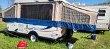 An extended RV rental pop-up camper with mesh windows on a grassy campsite. A red generator sits nearby.