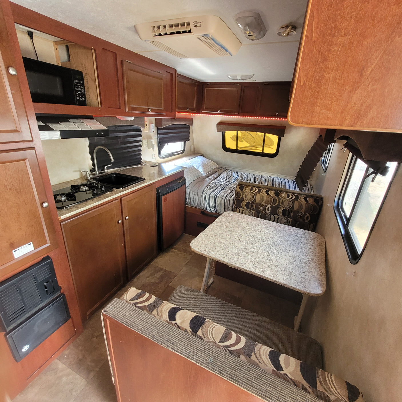 RV rental interior: modern kitchen, dinette with seating, and a bed. Ceiling AC & wood cabinetry visible.