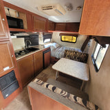 RV rental interior: modern kitchen, dinette with seating, and a bed. Ceiling AC & wood cabinetry visible.