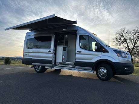 Explore this custom silver Ford Transit camper van RV rental with extended awning & visible interior.