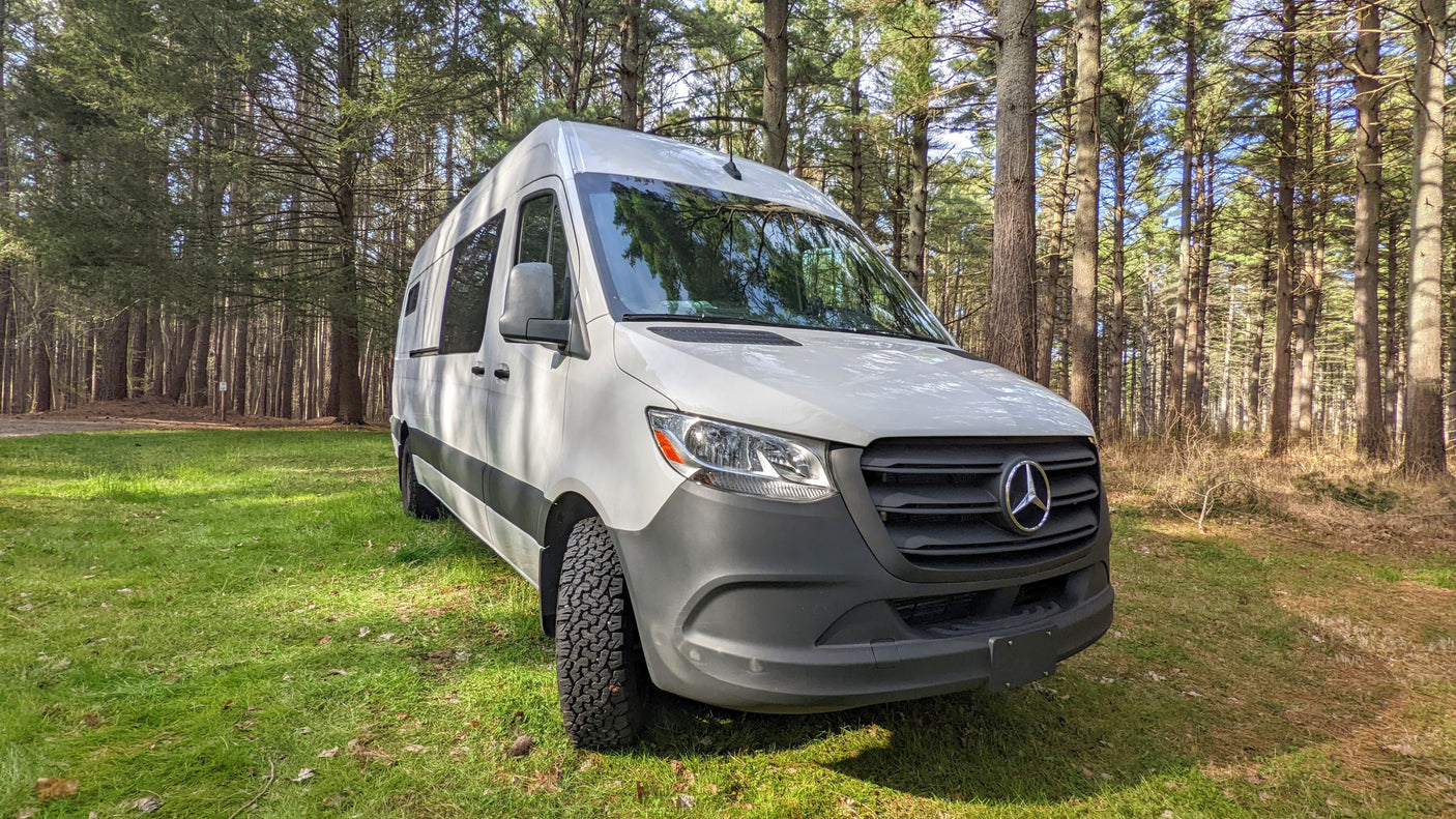 White Mercedes Sprinter camper van, an ideal RV rental for forest camping and nature adventures. Parked on grass.