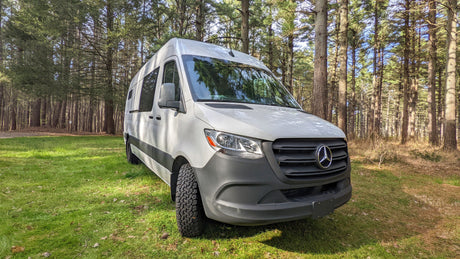 White Mercedes Sprinter camper van, an ideal RV rental for forest camping and nature adventures. Parked on grass.