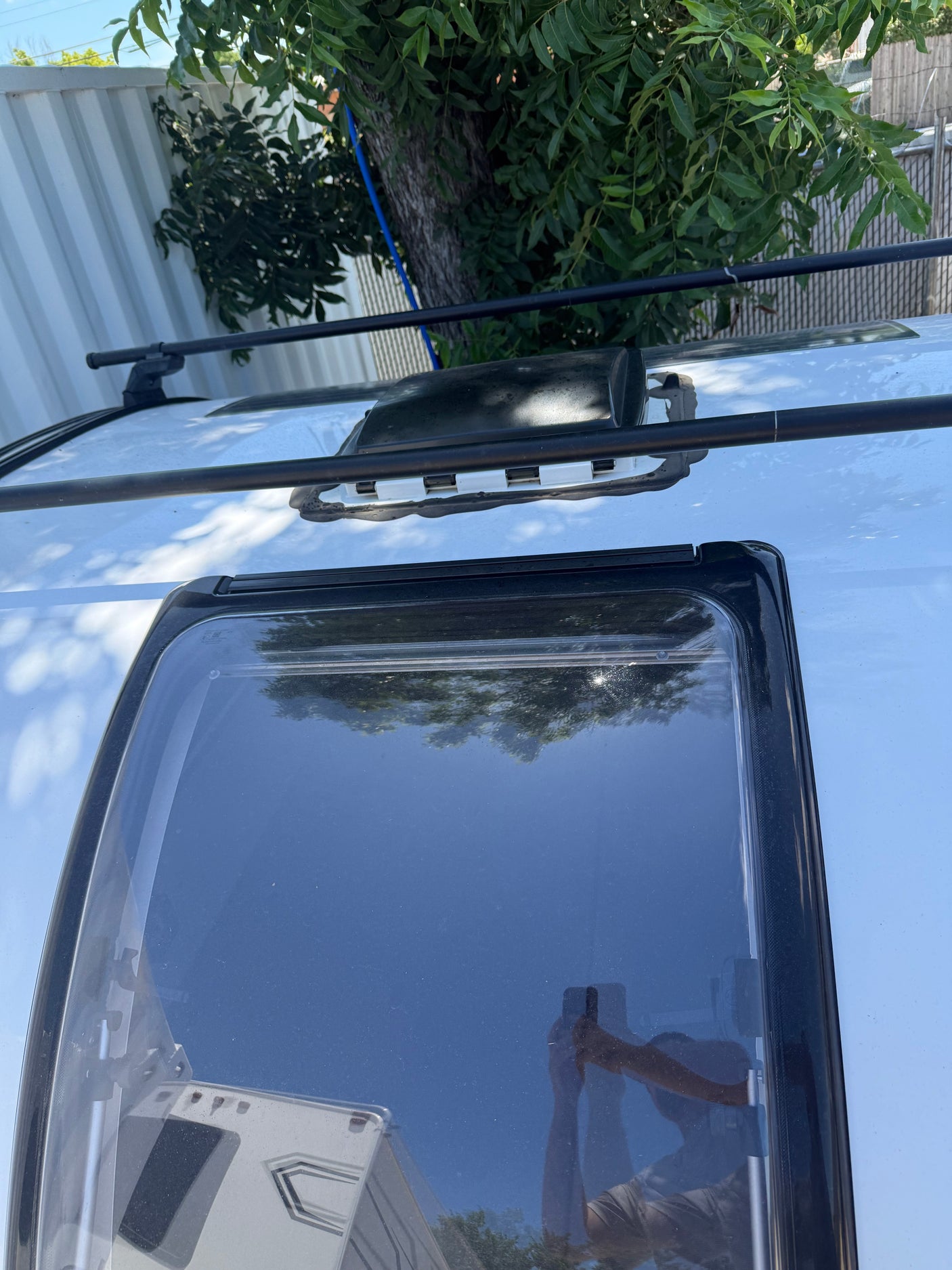 Top-down view of an RV rental roof with a large skylight, roof rack, and vent. Reflections show trees and sky.