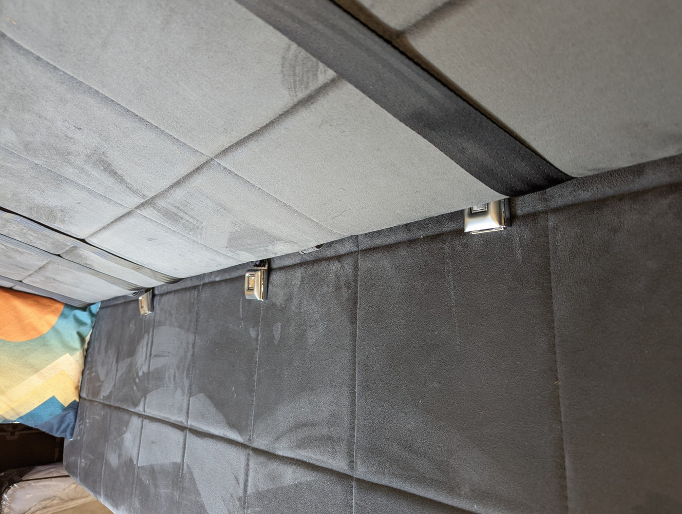 Upward view inside an RV rental: quilted grey panels, dark securing strap, and gleaming buckles. — photo 7