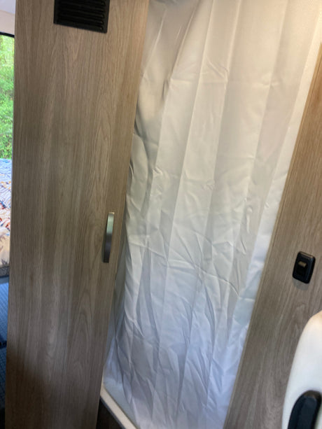 Inside an rv rental: a compact shower with white curtain and light wood-look partitions, practical for travel comfort.