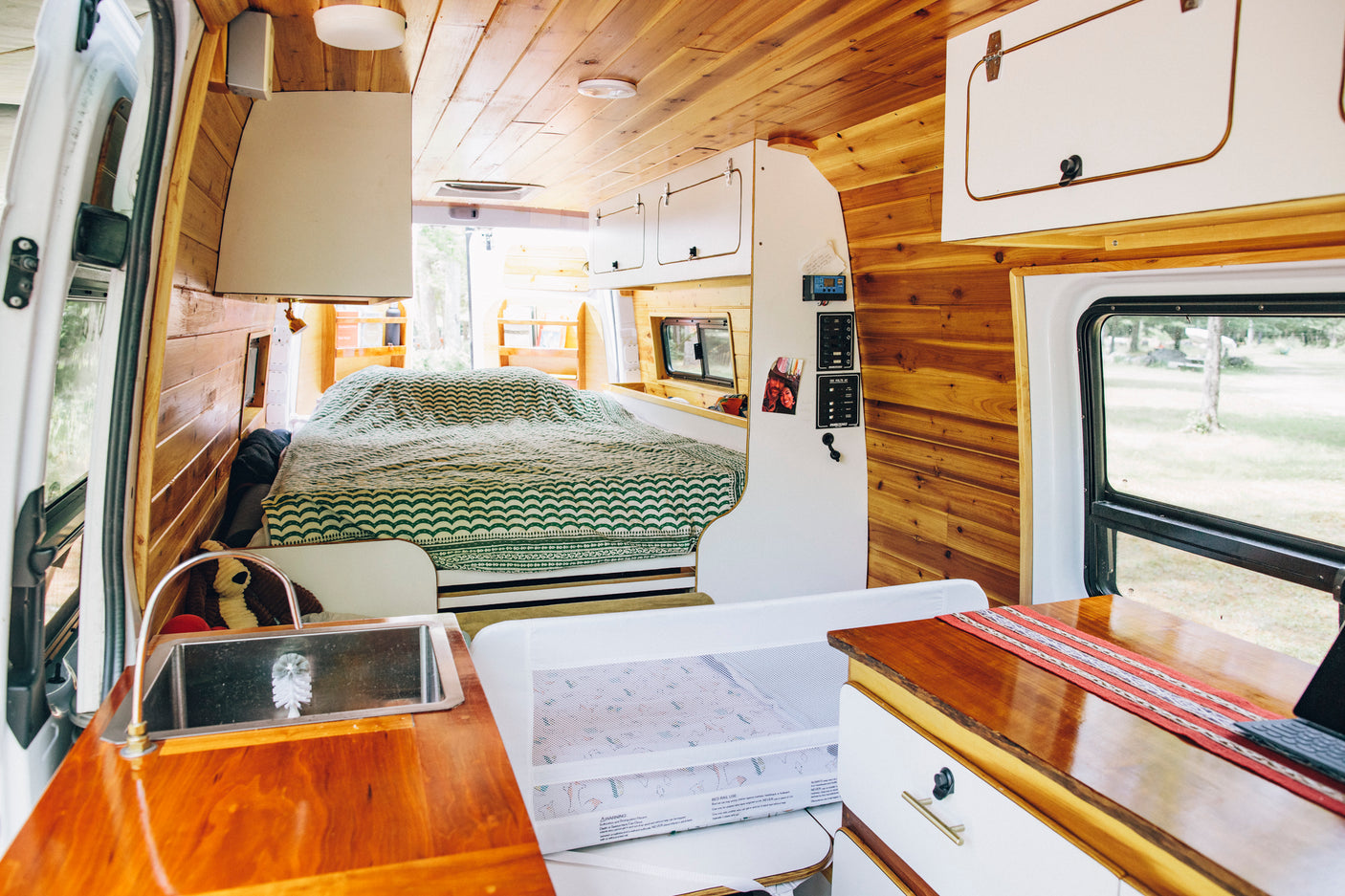 Cozy rv rental interior: wood-paneled walls, bed, kitchen, and baby sleep space for family travel adventures.