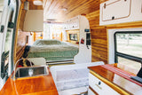 Cozy rv rental interior: wood-paneled walls, bed, kitchen, and baby sleep space for family travel adventures.