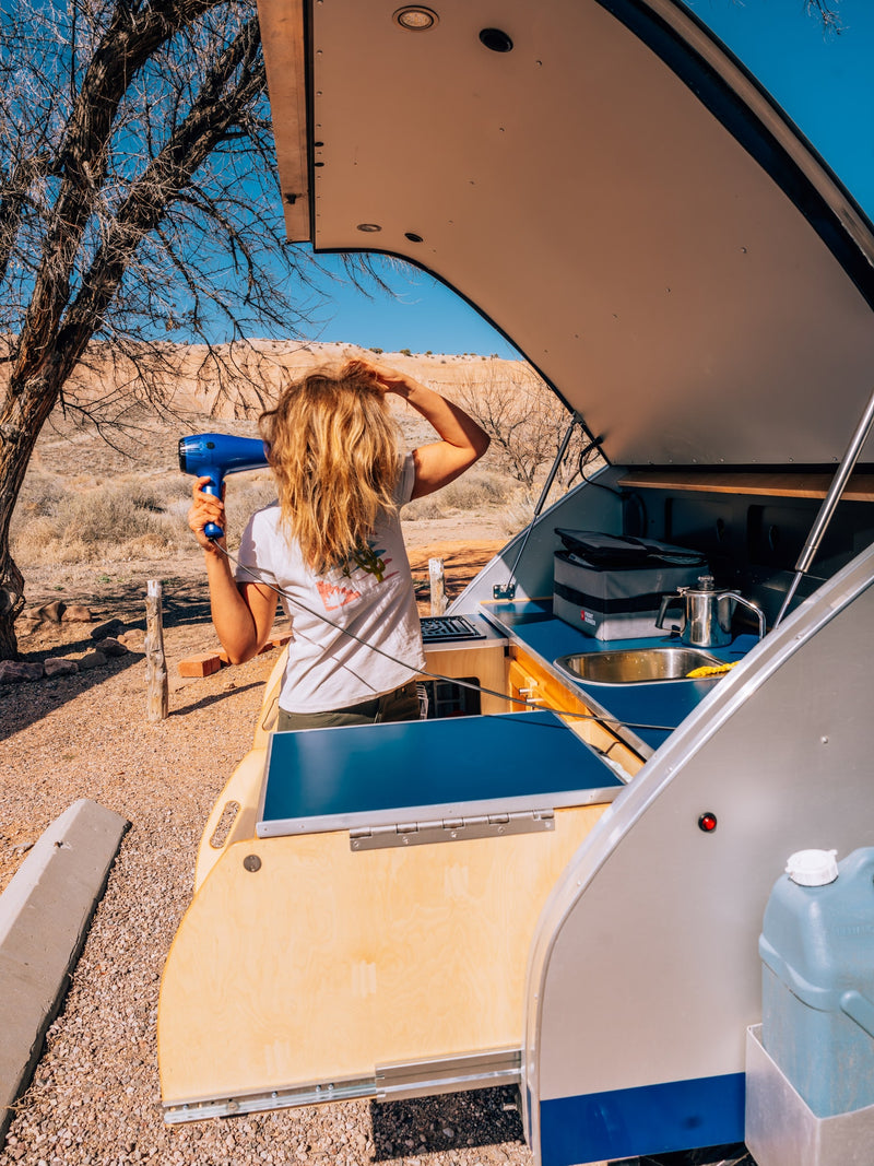 RV rental offers outdoor convenience! Woman dries hair at its compact kitchen in the desert. — photo 1