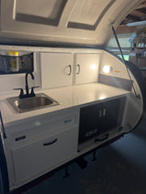Compact RV rental kitchen with sink, faucet, white cabinets, countertop, and ICECO cooler.