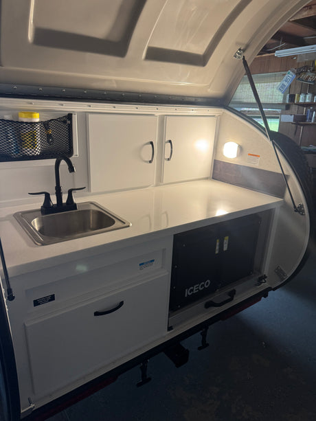 Compact RV rental kitchen with sink, faucet, white cabinets, countertop, and ICECO cooler.