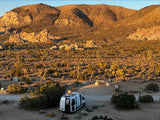 RV rental parked at a desert campsite among Joshua trees and mountains at golden hour. Perfect for a nature retreat.