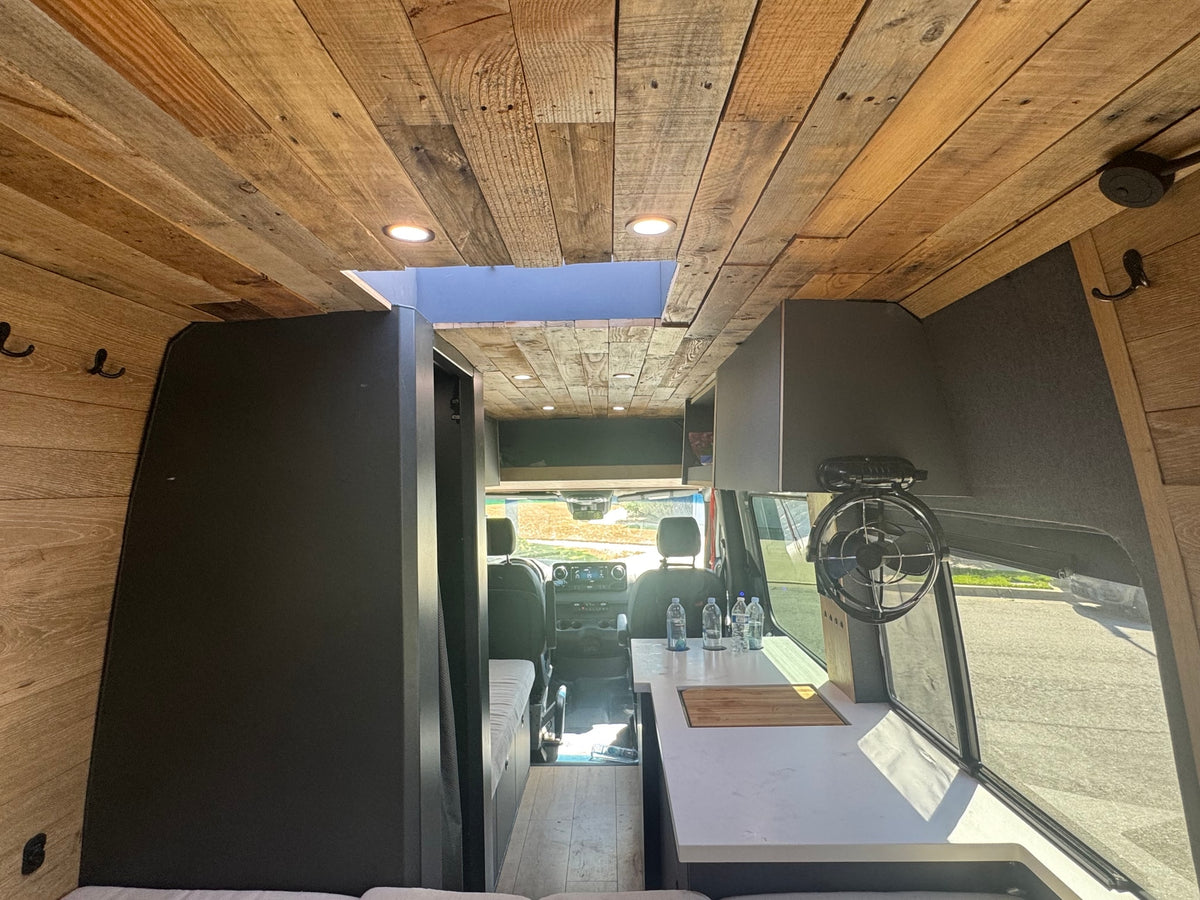 Cozy rv rental interior with a reclaimed wood ceiling, skylight, and kitchen area, looking towards the cockpit. — photo 5