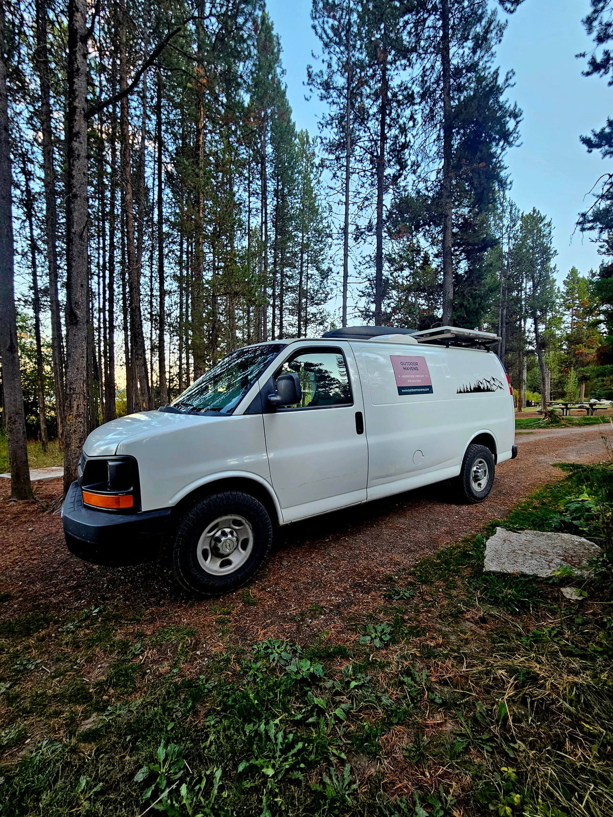 White campervan for RV rental parked in a pine forest campground — photo 1