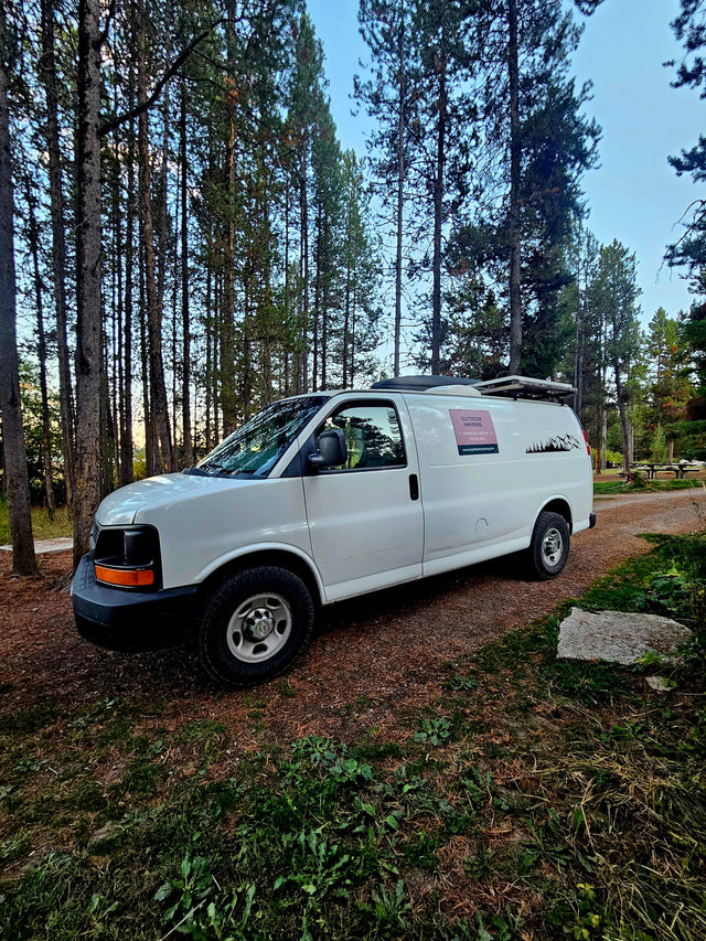 White campervan for RV rental parked in a pine forest campground