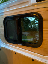 RV rental van conversion: a wood-paneled interior wall features a window, reflecting a residential street outside.