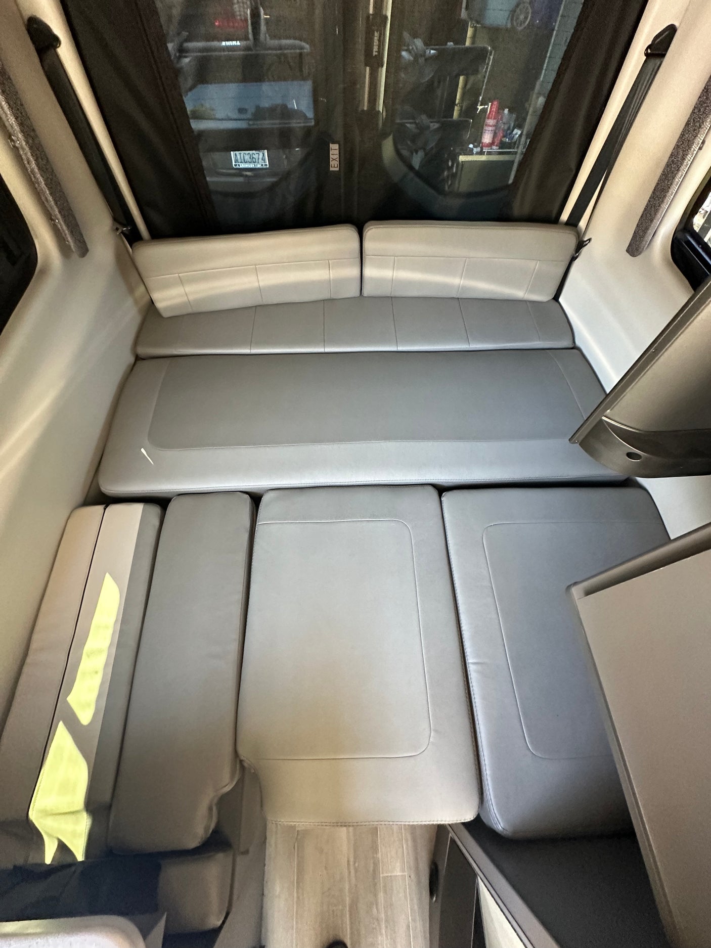 RV rental interior: Versatile grey cushioned seating converts to a bed. Ideal for travel, with exterior view and license plate.