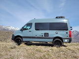 Explore with this light blue Sanctuary RV rental van, parked on a hill with impressive snow-capped mountains in the background.