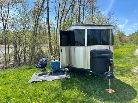 A silver Airstream travel trailer (RV rental) with an outdoor seating area by a pond on a sunny day.