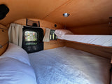 Cozy RV rental interior with wooden walls and ceiling, featuring comfortable bunk beds, a window, and fans for comfort.