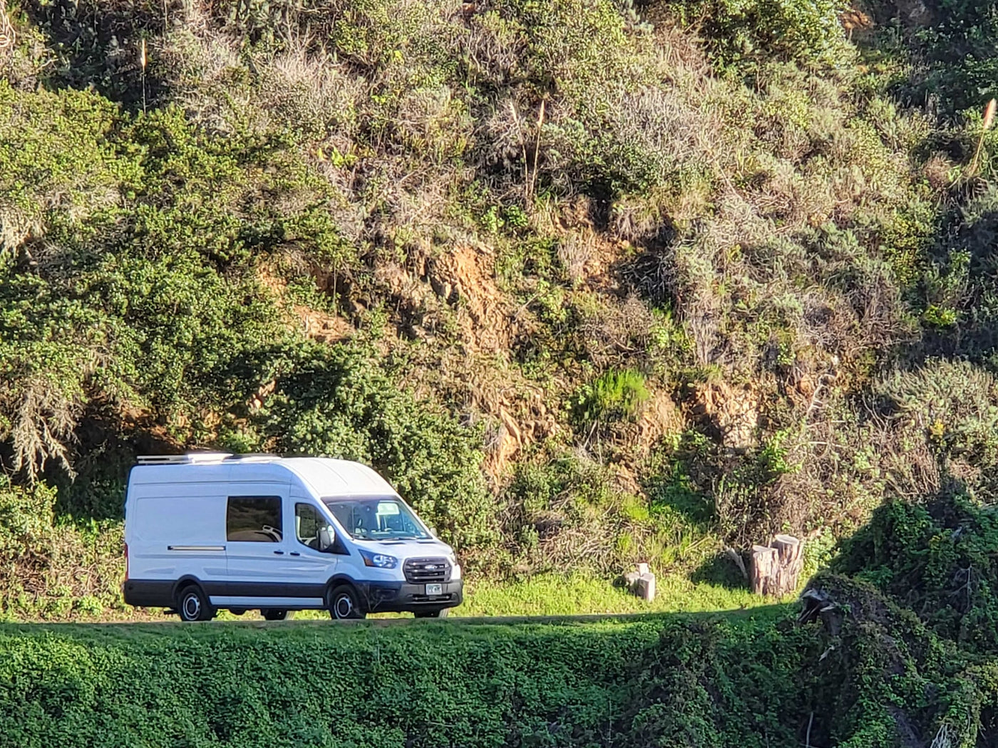 White RV rental van on a scenic road with vibrant green, sunlit hills. An ideal ride for travel and outdoor adventures. — photo 18