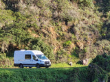 White RV rental van on a scenic road with vibrant green, sunlit hills. An ideal ride for travel and outdoor adventures.