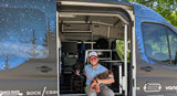 A man and his two dogs pose inside a spacious RV rental van with custom starry night wrap, ideal for outdoor trips.