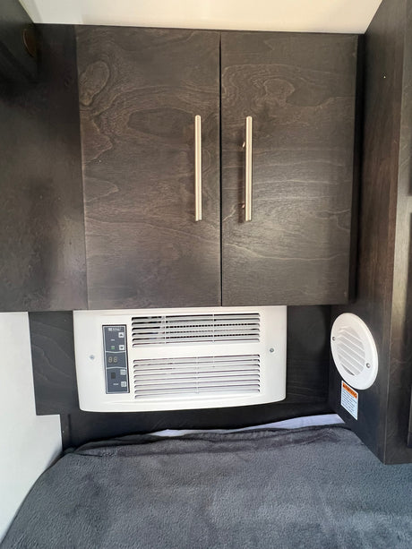 RV rental bedroom with dark wood cabinets, an air conditioner, and a cozy gray blanket on the bed.