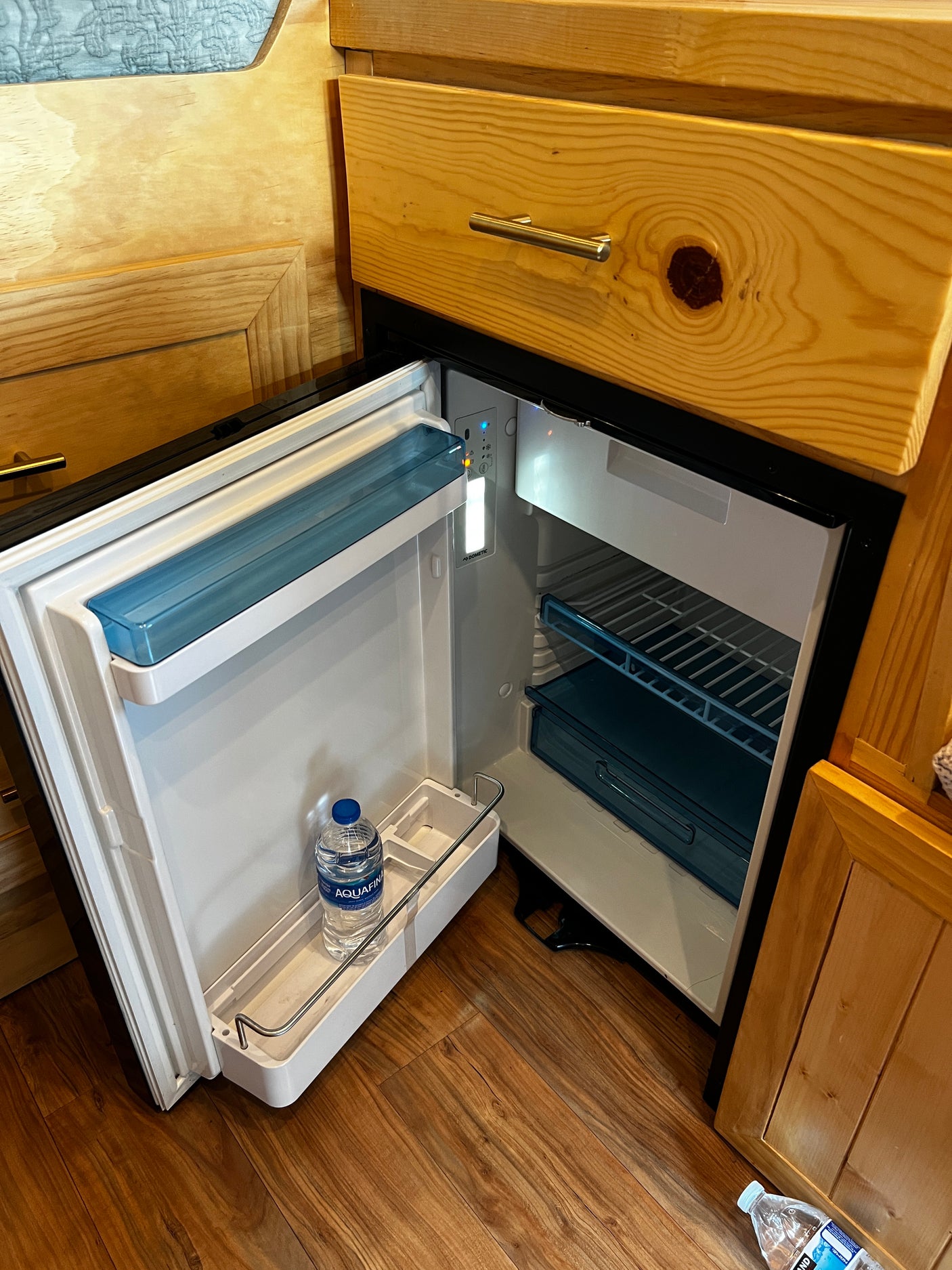 Compact, open mini-fridge in an RV rental, showing interior shelves and an Aquafina water bottle.