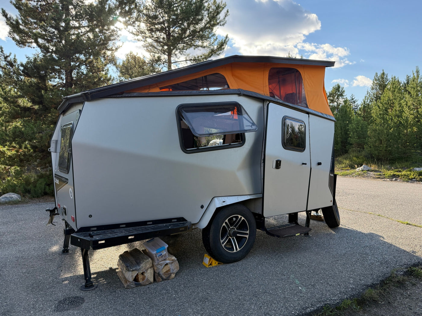 This silver rv rental pop-top travel trailer with an orange tent is parked on asphalt, ready for outdoor adventure amidst trees. — photo 3
