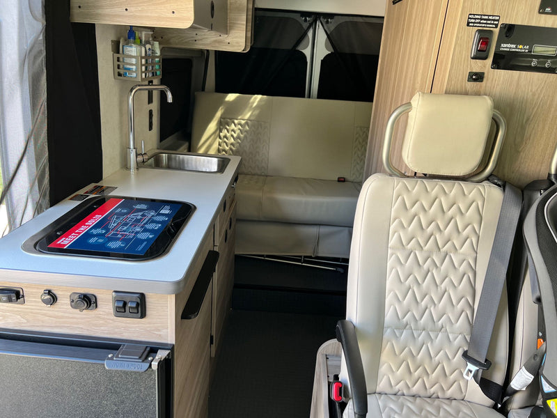  and window view.|Inside a comfy RV rental: A neat bed with white sheets and pillows next to windows showing a bright green outdoor scene. Ideal for travel rest.|Inside an RV rental pop-top: a comfy bed with white linens and a Purdue Boilermakers blanket — photo 10