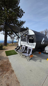 An rv rental, a Go Lite travel trailer, is set up with an awning and chairs on a concrete pad, overlooking a scenic mountain vista.