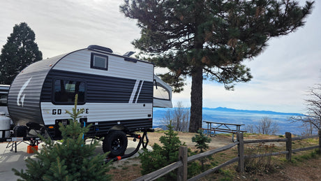 Experience outdoor living! An rv rental, modern camper with pop-out, overlooks a vast mountain landscape from a scenic campsite.