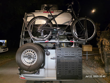RV rental: A silver Mercedes van's rear shows a bike, spare tire, & side storage. Night scene, ready for adventure.