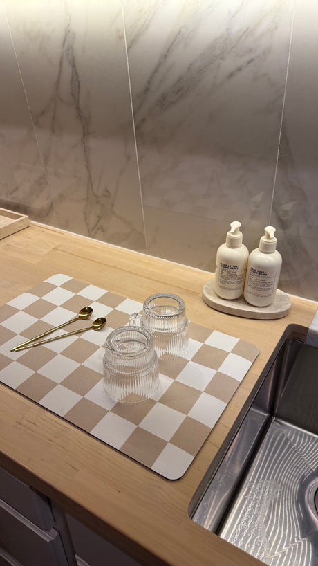 Compact kitchen setup in an RV rental. Features a modern sink, light wood counter, and checkered dish drying mat with glassware.